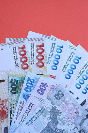 Argentine pesos money bills in big amount lies on red color table close up. Finance and banking conceptの写真素材
