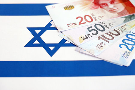 Israel New Shekels banknotes on national flag. The current Israel money bills lies on flag in big amount. The concept of business and investment in Israelの写真素材