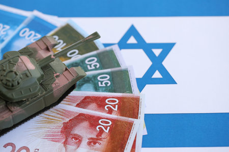Israel New Shekels banknotes and toy tank on flag. The current Israel money bills and tank lies on...
