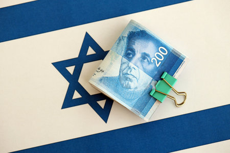 Israel New Shekels banknotes on national flag. The current Israel money bills lies on flag in big amount. The concept of business and investment in Israelの写真素材