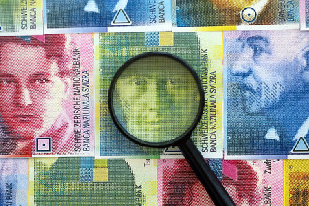Swiss franc banknotes and magnifying glass. The francs money bills with loupe lies on table in big amount. The concept of financial monitoring and taxation in Switzerlandの写真素材