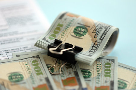 Big amount of United States dollar bills on table with individual income tax return form close up. Concept of taxation and accounting in United Statesの写真素材