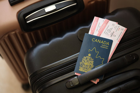 Canadian passport with tickets lies on touristic suitcase close up in airport waiting hall. Travel worldwide and international tourism conceptの写真素材