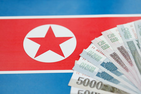 North Korean won money bills in big amount lies on People Republic of Korea flag close up. Finance...