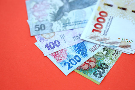 Argentine pesos money bills in big amount lies on red color table close up. Finance and banking conceptの写真素材