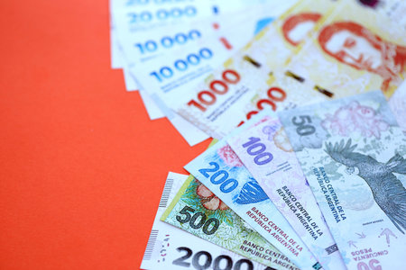 Argentine pesos money bills in big amount lies on red color table close up. Finance and banking conceptの写真素材