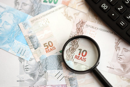 Brazilian reais banknotes and calculator with magnifying glass. The current Brazil real money bills and calc with loupe lies on table in big amount. The concept of taxation and money count in Brazilの写真素材