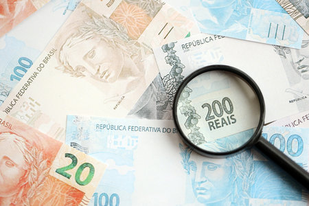 Brazilian reais banknotes and magnifying glass. The current Brazil real money bills and loupe lies on table in big amount. The concept of financial monitoring and taxation in Brazilの写真素材