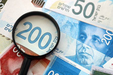 Israel New Shekels banknotes and magnifying glass. The current Israel money bills with loupe lies on...