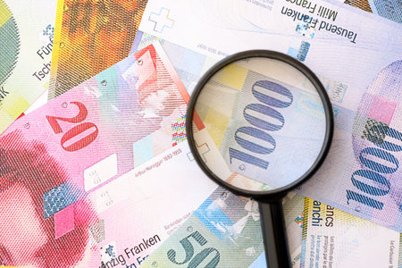 Swiss franc banknotes and magnifying glass. The current francs money bills with loupe lies on table in big amount. The concept of financial monitoring and taxation in Switzerlandの写真素材