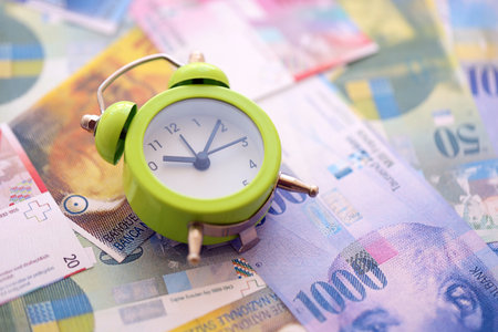 Swiss franc banknotes and alarm clock. The current francs money bills and clock lies on table in big amount. The concept of time management and income in Switzerlandの写真素材