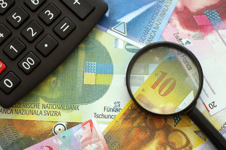Swiss franc banknotes and calculator with magnifying glass. The current francs money bills and calc with loupe lies on table in big amount. The concept of taxation and business in Switzerlandの写真素材