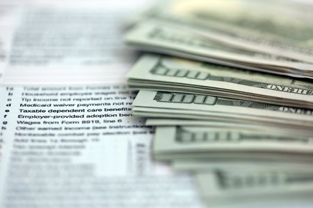 Big amount of United States dollar bills on table with individual income tax return form close up. Concept of taxation and accounting in United Statesの写真素材