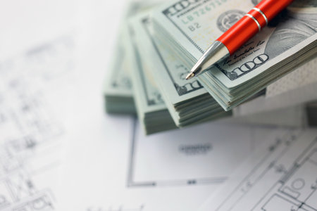 Big amount of US dollars money bills with pen and planning blueprints of residential building project close up. Investment and construction project conceptの写真素材