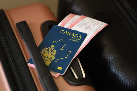Canadian passport with tickets lies on touristic suitcase close up in airport waiting hall. Travel worldwide and international tourism conceptの写真素材