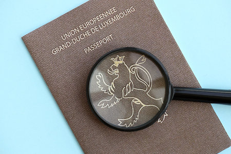 Luxembourg passport and magnifying glass on light blue paper background close up. Citizenship...