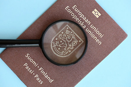 Finland passport and magnifying glass on light blue paper background close up. Citizenship details and information conceptの写真素材