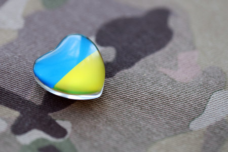 Glass heart with Ukrainian flag colors lies on military camouflage fabric. Concept of support and defend Ukraineの写真素材