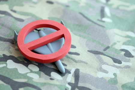 Unnamed grey toy drone and red prohibition sign on camouflage fabric close up. Anti-aircraft warfare conceptの写真素材