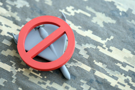 Unnamed grey toy drone and red prohibition sign on camouflage fabric close up. Anti-aircraft warfare conceptの写真素材