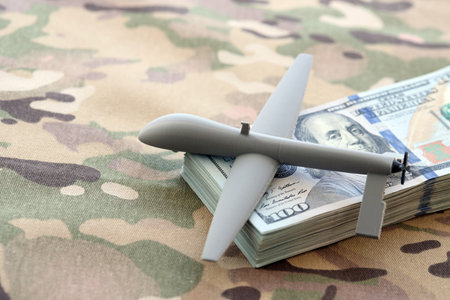 Unnamed grey toy drone model and dollar bills on camouflage fabric close up.の写真素材
