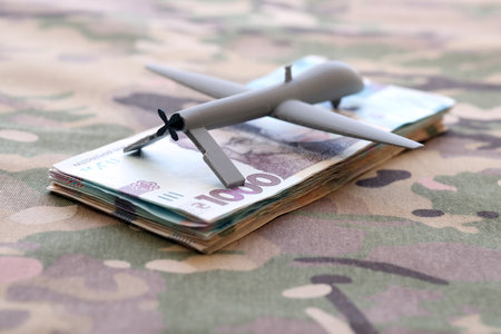 Unnamed grey toy drone model and money bills on camouflage fabric close up.の写真素材