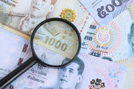 Thai baht currency money bills and magnifying glass close up. The concept of financial monitoring and taxationの写真素材