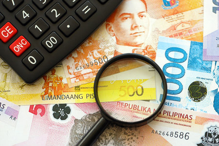 Philippines peso currency money bills and calculator with magnifying glass close up. The concept of taxation and money countの写真素材