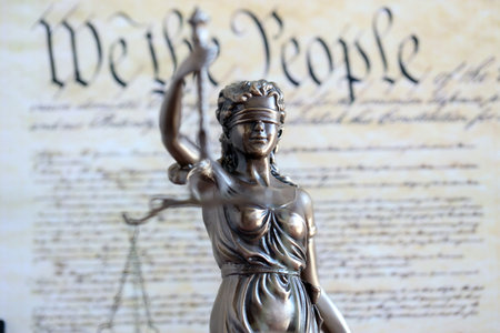Lady Justice bronze statue on background of US Constitution page close up. Lawsuit and punishment in United States of Americaの写真素材