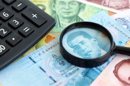 Thai baht currency money bills and calculator with magnifying glass close up. The concept of taxation and money countの写真素材
