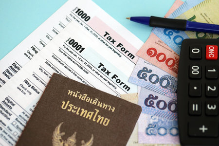 Thai baht money bills and calculator with tax form close up on blue. Taxation and accounting conceptの写真素材