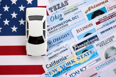 Toy car on big amount of driving licenses from different USA states on flag close up. Stack of driving license specimen cardsの写真素材