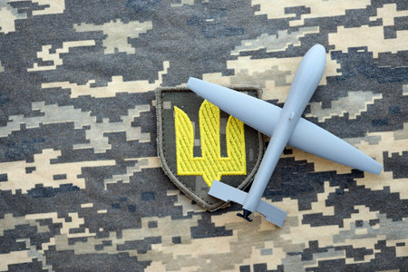 Unnamed grey toy drone model and Ukrainian Armed Force patch on camouflage fabric close upの写真素材