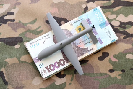 Unnamed grey toy drone model and money bills on camouflage fabric close up. Drone manufacturing fundsの写真素材