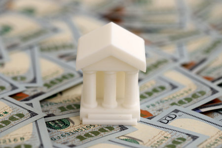 White toy bank on big amount of US dollar bills close up. Business and banking concept