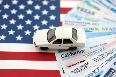 Toy car on big amount of driving licenses from different USA states on flag close up. Stack of driving license specimen cardsの写真素材