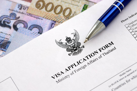 Visa application form to enter Thailand on table with pen and thai money bills close upの写真素材