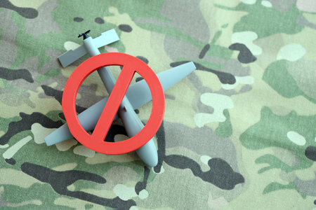 Unnamed grey toy drone model and red prohibition sign on camouflage fabric close up. Anti-aircraft warfare conceptの写真素材