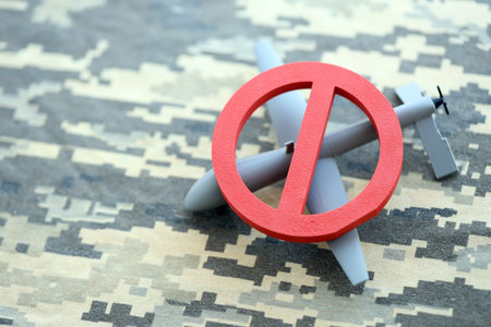 Unnamed grey toy drone model and red prohibition sign on camouflage fabric close up. Anti-aircraft...