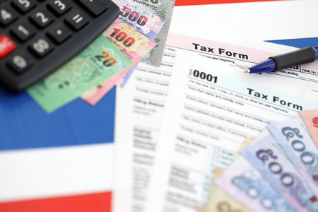 Thai baht money bills and calculator with tax form on flag close up. Taxation and accounting conceptの写真素材