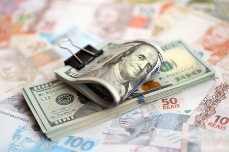 Bunch of US dollar bills lies on big amount of Brazilian reais banknotes close up. American money bunch lies on Brazil money bills. The concept of economics and currency exchange in Brazilの写真素材