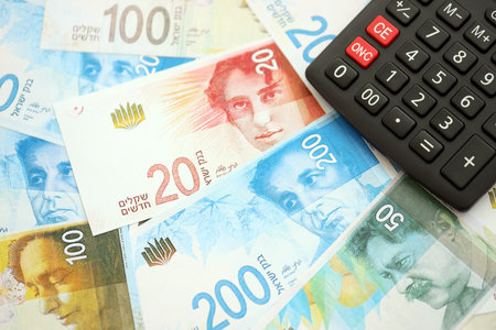 Israel New Shekels banknotes and calculator. The current Israel money bills and calc lies on table in big amount. The concept of taxation and money count in Israelの写真素材