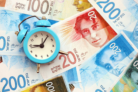 Israel New Shekels banknotes and alarm clock. The current Israel money bills and clock lies on table...