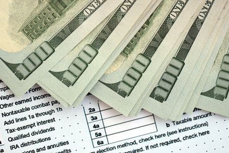 Big amount of United States dollar bills on table with individual income tax return form close up. Concept of taxation and accounting in United Statesの写真素材