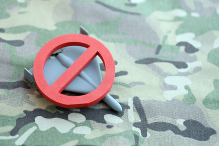 Unnamed grey toy drone and red prohibition sign on camouflage fabric close up. Anti-aircraft warfare conceptの写真素材