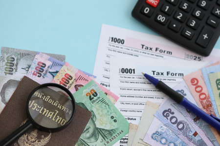 Thai baht money bills and calculator with tax form close up on blue. Taxation and accounting conceptの写真素材