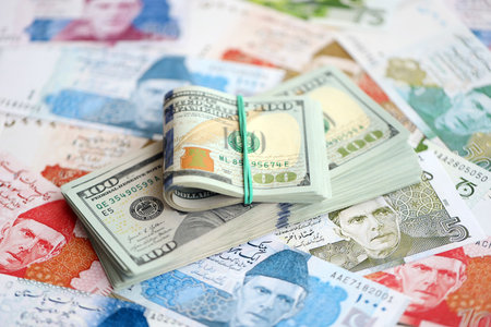 Stack of US dollar bills lies on big amount of Pakistan rupees banknotes close up. American money...