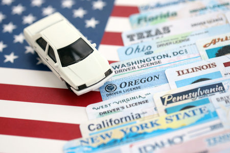 Toy car on big amount of driving licenses from different USA states on flag close up. Stack of driving license specimen cardsの写真素材