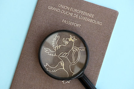 Luxembourg passport and magnifying glass on light blue paper background close up. Citizenship details and information conceptの写真素材