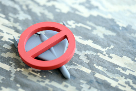Unnamed grey toy drone and red prohibition sign on camouflage fabric close up. Anti-aircraft warfare conceptの写真素材
